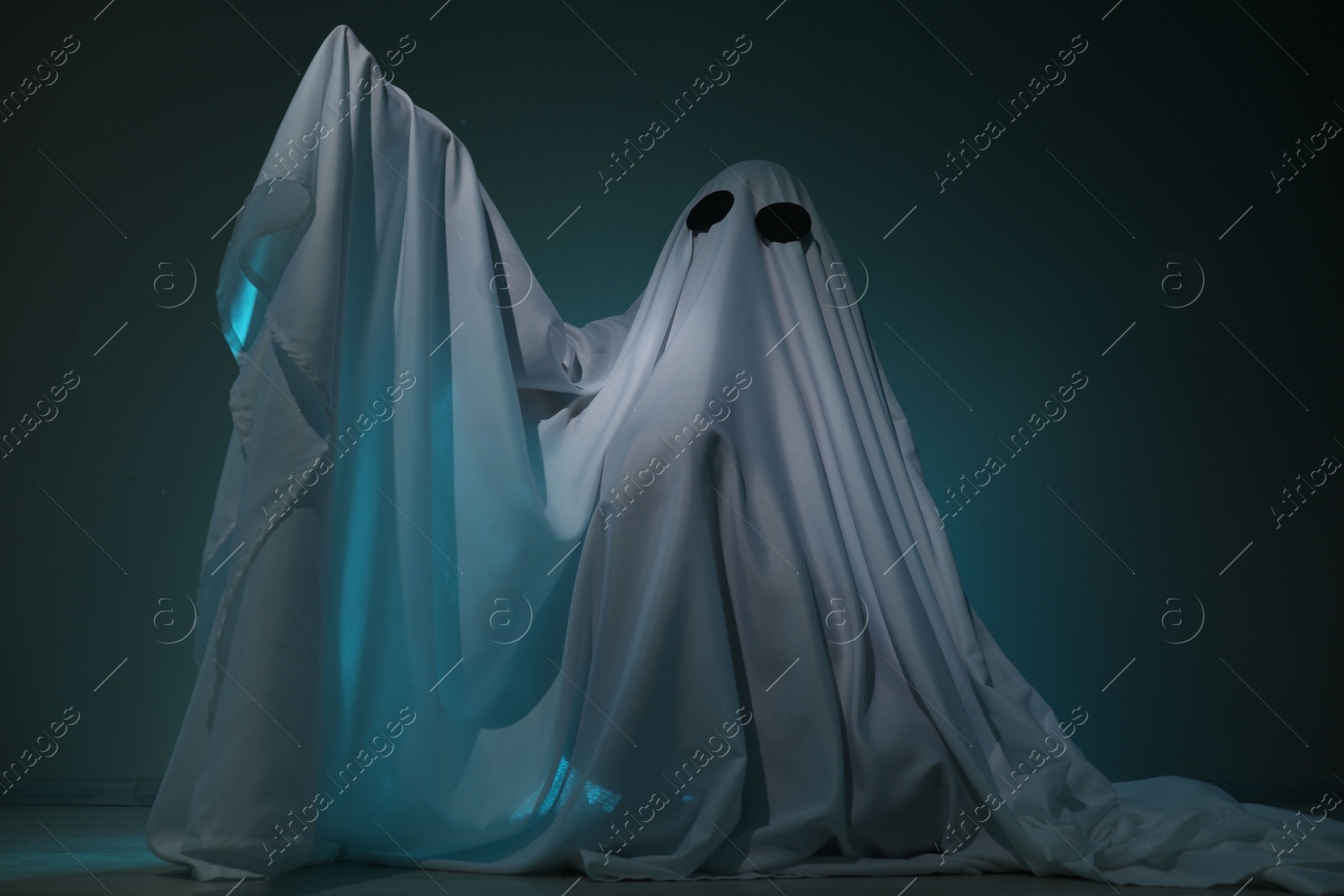 Photo of Creepy ghost. Woman covered with sheet on dark teal background