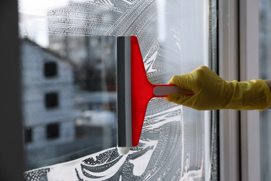 Woman cleaning window with squeegee indoors, closeup