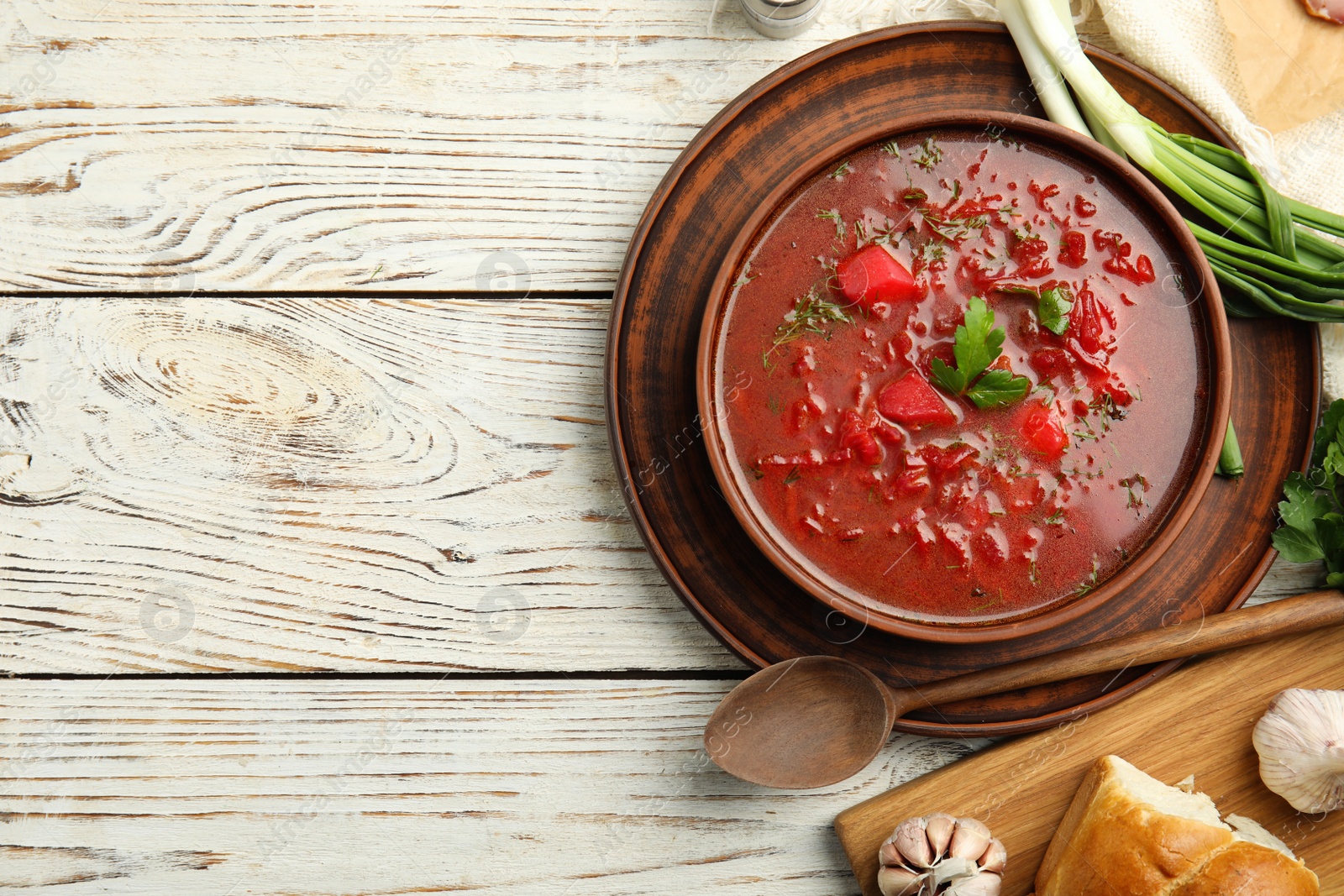 Photo of Stylish brown clay bowl with Ukrainian borsch served on white wooden table, flat lay. Space for text