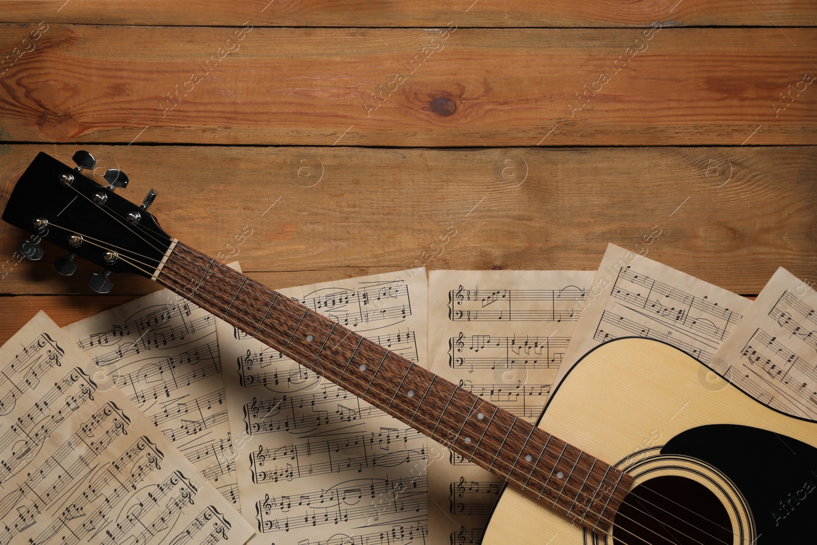 Photo of Paper sheets with music notes and acoustic guitar on wooden table, top view