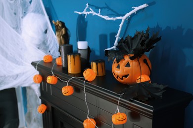 Jack-o'-lantern lights and different Halloween decorations on black fireplace near blue wall