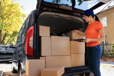 Photo of Courier counting packages near delivery truck outdoors