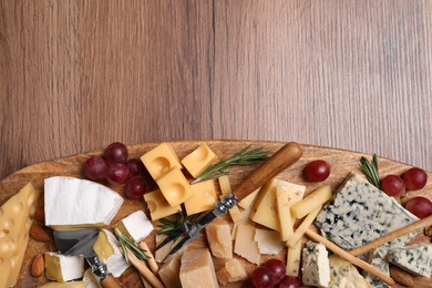 Photo of Cheese plate with rosemary, grapes and nuts on wooden table, top view. Space for text