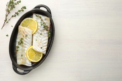 Photo of Fresh raw cod fillets with thyme and lemon in baking dish on white wooden table, top view. Space for text
