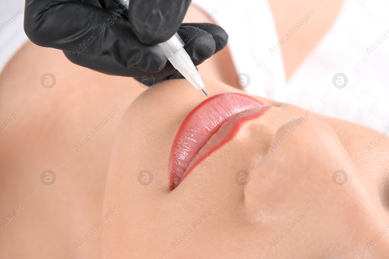 Photo of Young woman getting permanent makeup on lips in beautician salon, closeup