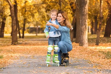 Mother and her daughter wearing roller skates in autumn park