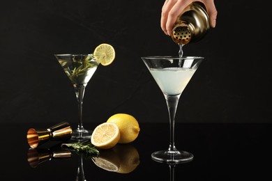 Photo of Woman pouring Martini cocktail into glass on black background, closeup