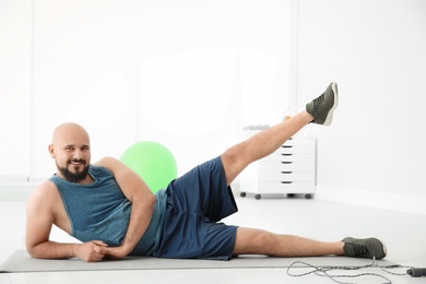 Overweight man doing exercise on mat in gym