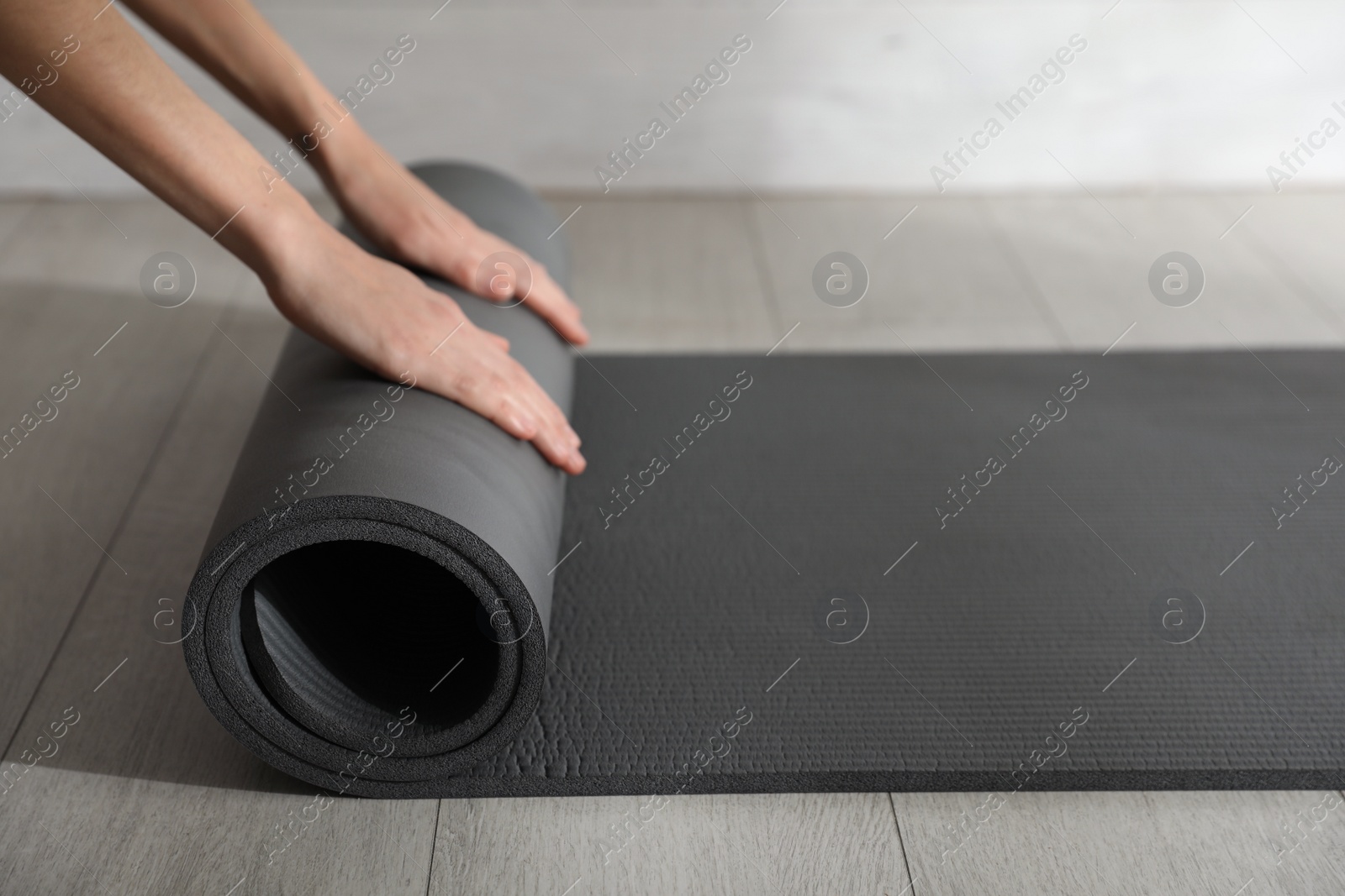 Photo of Woman rolling black yoga mat on floor indoors, closeup