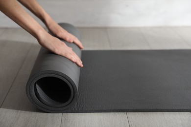 Photo of Woman rolling black yoga mat on floor indoors, closeup
