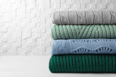 Photo of Stack of warm clothes on white wooden table against textured wall. Autumn season