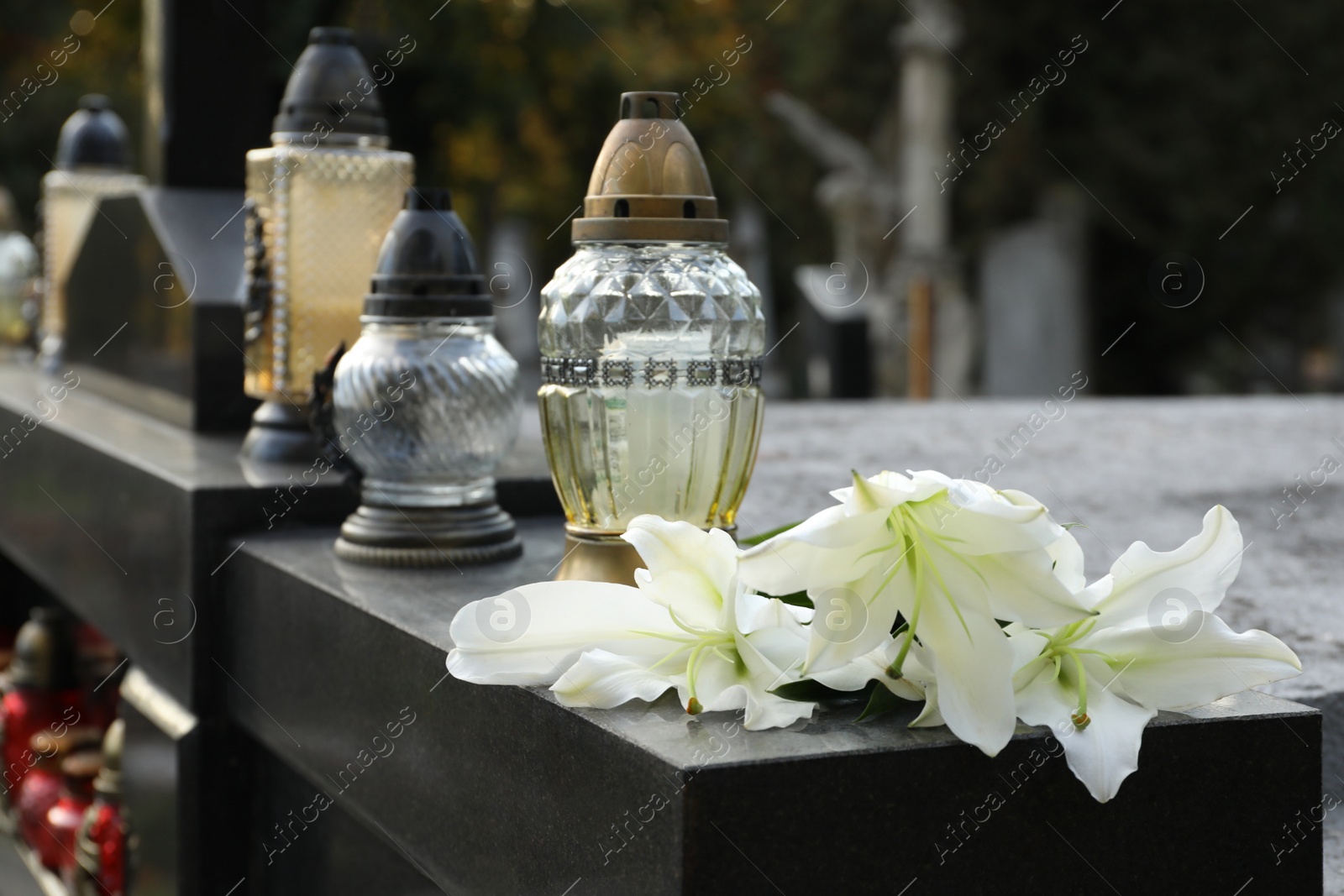 Photo of White lilies and grave light on granite tombstone outdoors, space for text. Funeral ceremony