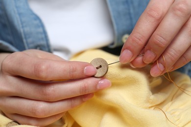 Photo of Woman sewing button with needle and thread onto shirt, closeup