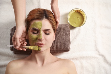 Photo of Cosmetologist applying mask onto woman's face in spa salon, top view. Space for text