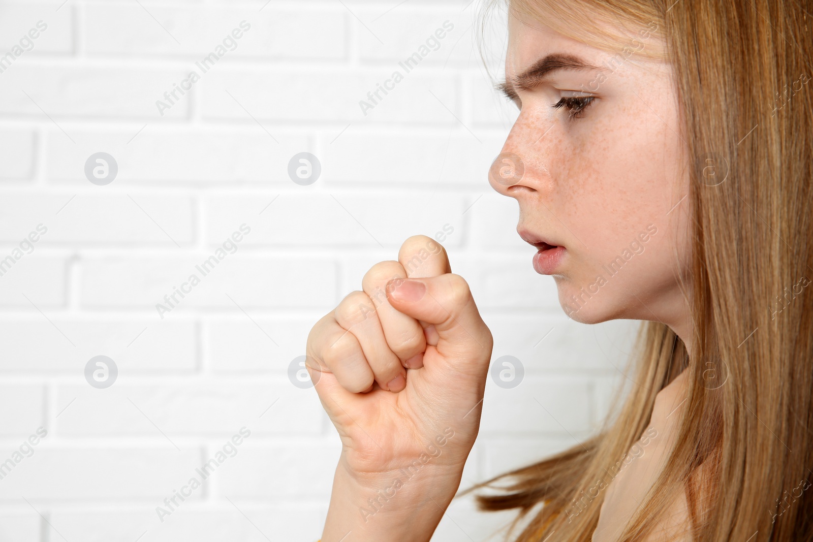 Photo of Teenage girl suffering from cough near brick wall. Space for text