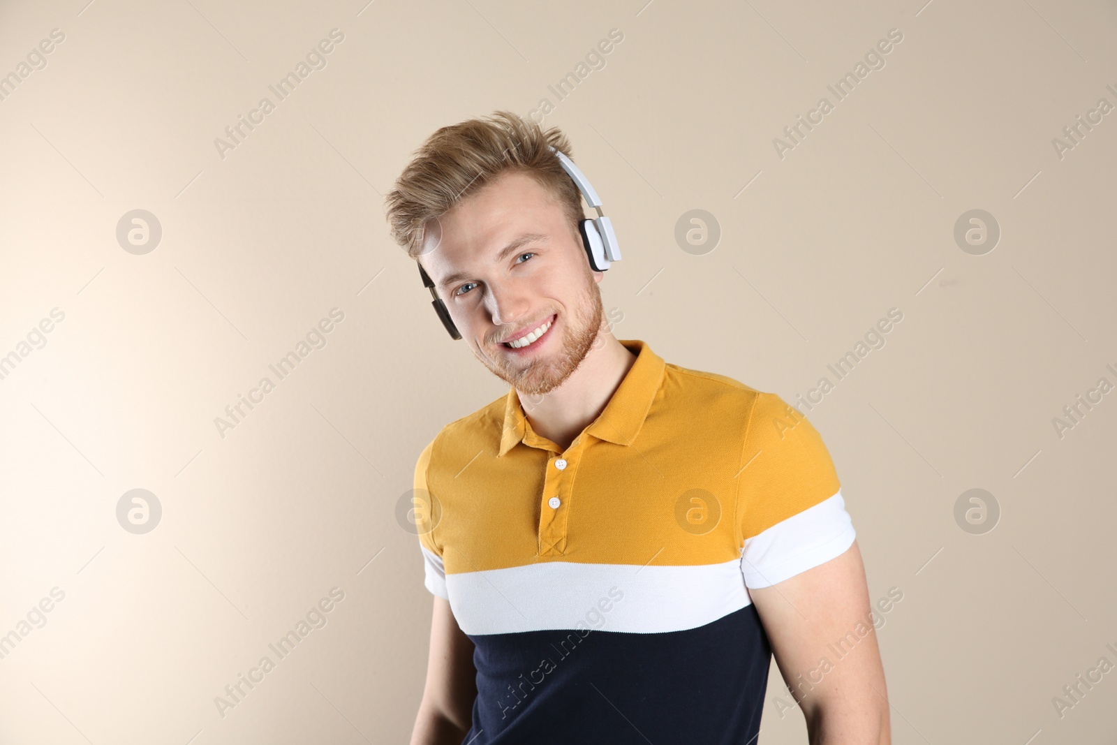 Photo of Handsome young man listening to music with headphones on color background