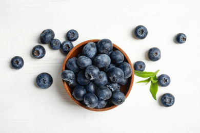 Fresh ripe blueberries in bowl on white wooden table, flat lay