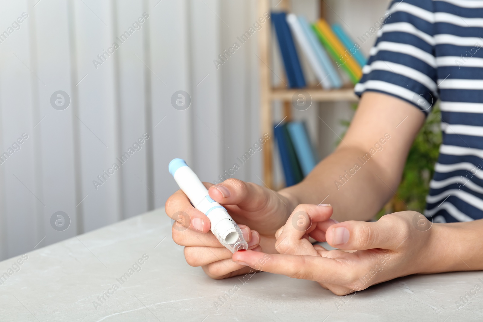 Photo of Woman using lancet pen at table. Diabetes test