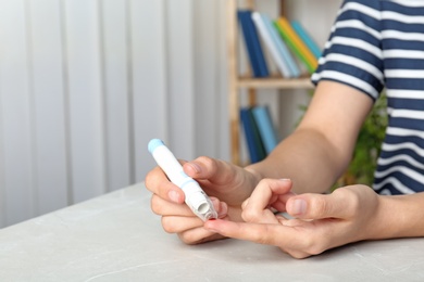 Woman using lancet pen at table. Diabetes test