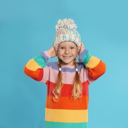 Photo of Cute little girl in warm hat and sweater on blue background. Winter season