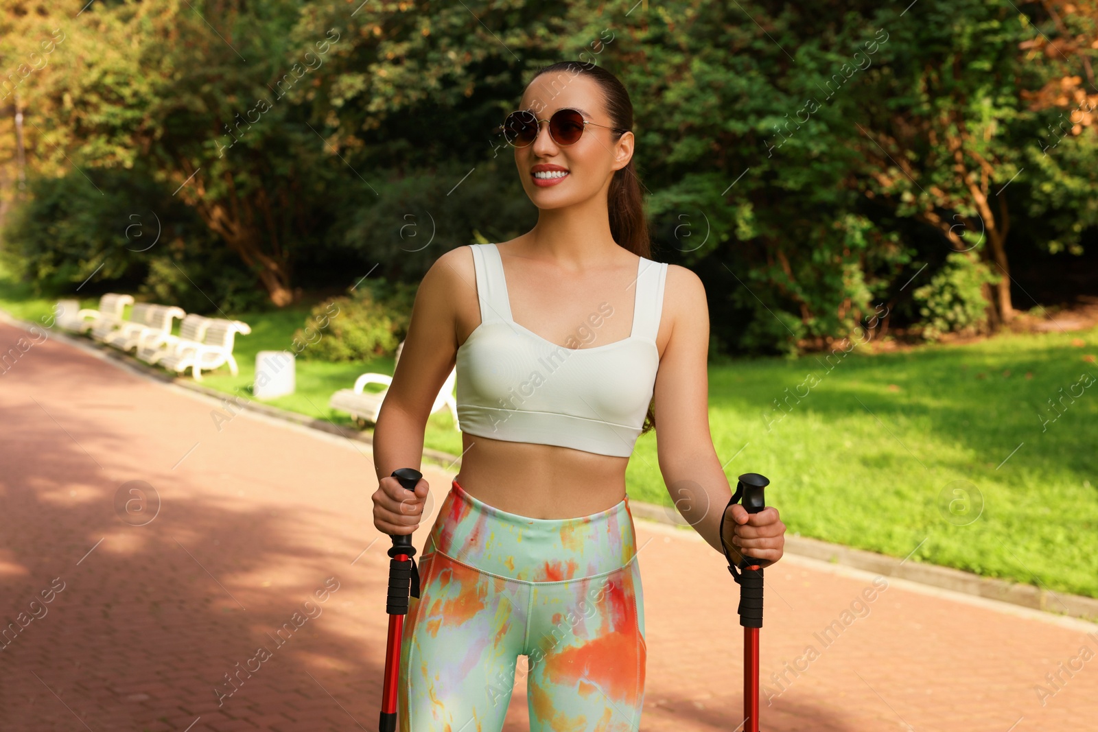 Photo of Young woman practicing Nordic walking with poles outdoors