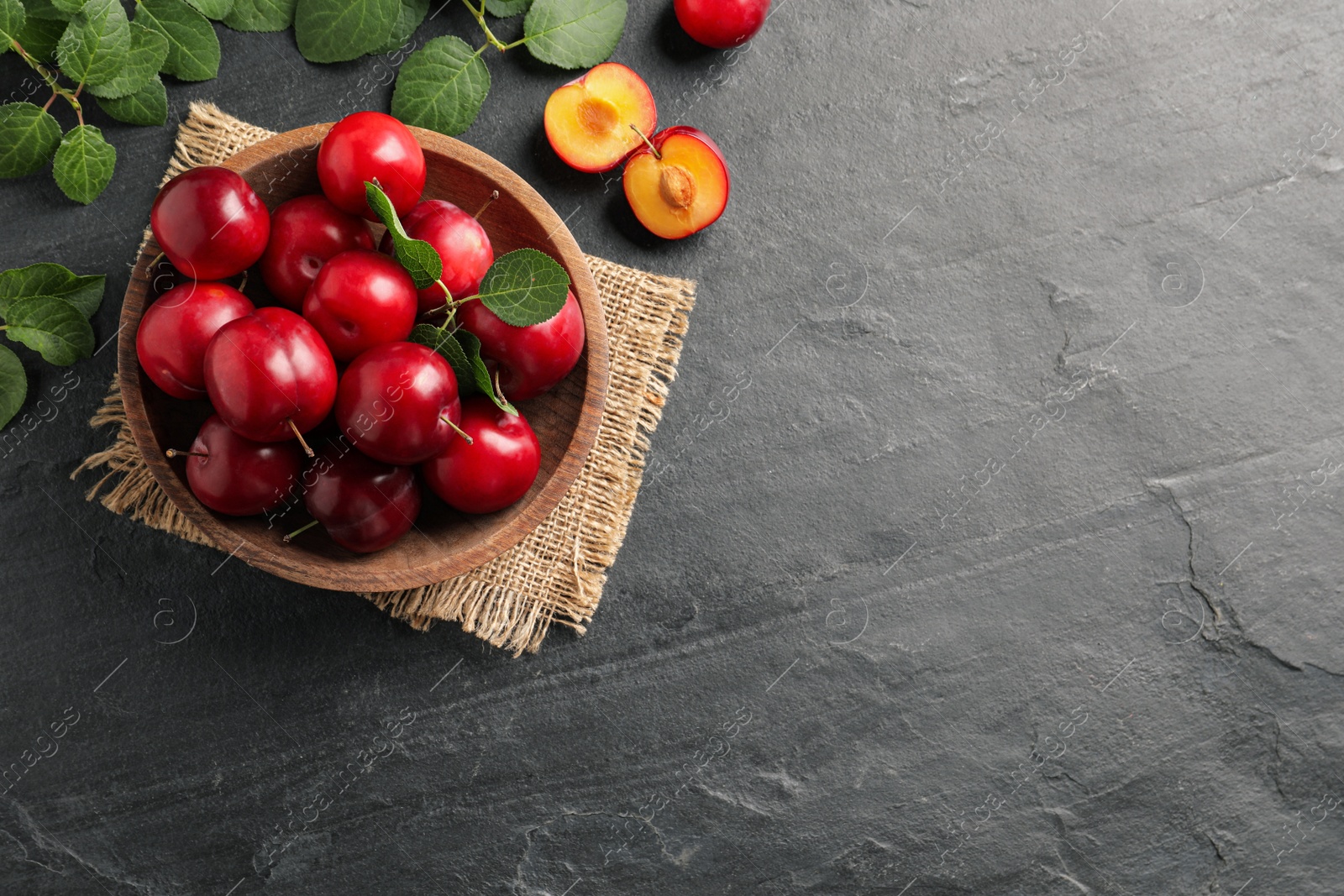 Photo of Delicious ripe cherry plums with leaves on black table, flat lay. Space for text