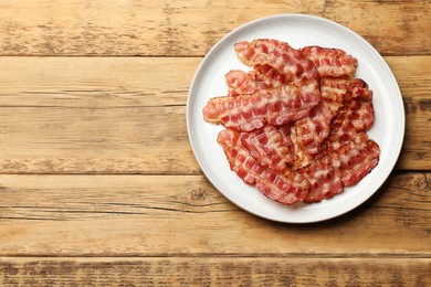 Photo of Plate with fried bacon slices on wooden table, top view. Space for text
