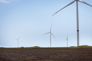 Photo of Modern wind turbine in field against blue sky. Energy efficiency