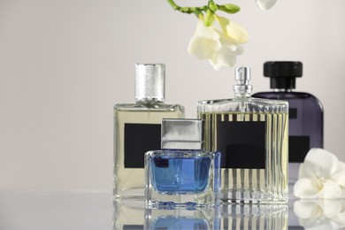 Luxury perfumes and freesia flowers on mirror surface against light grey background, space for text. Floral fragrance