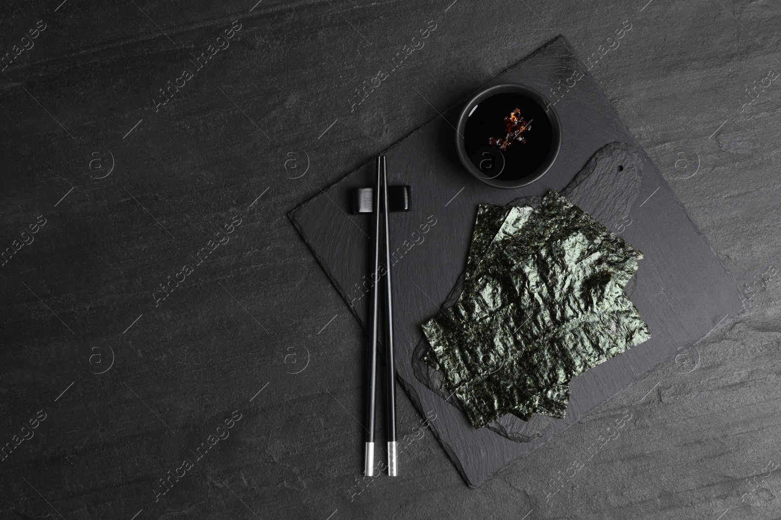 Photo of Dry nori sheets, soy sauce and chopsticks on black table, flat lay. Space for text