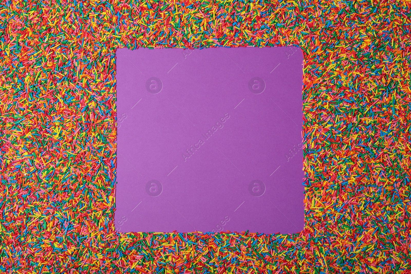 Photo of Frame of sprinkles on purple background, flat lay with space for text. Confectionery decor