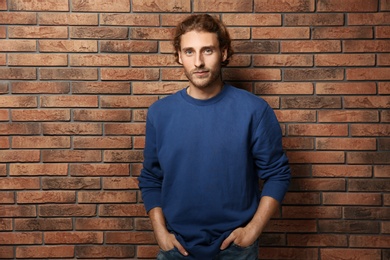 Photo of Handsome young man in warm sweater near brick wall