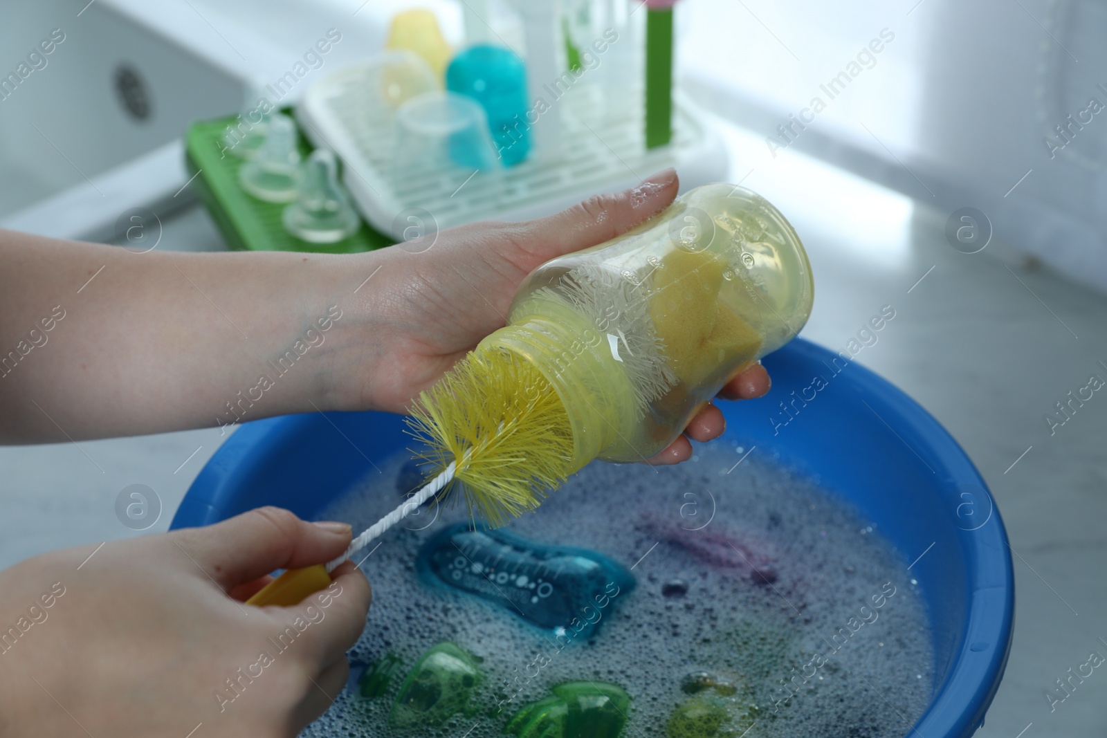 Photo of Woman washing baby bottle above basin in kitchen, closeup