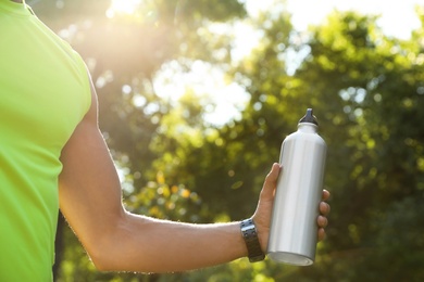 Photo of Young man holding bottle of water in park on sunny day, closeup
