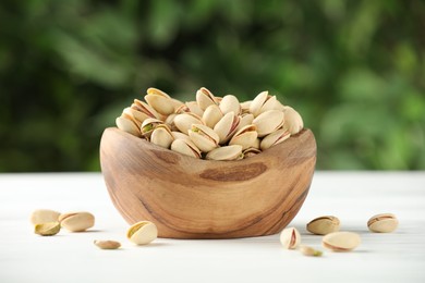 Photo of Tasty pistachios in bowl on white table against blurred background