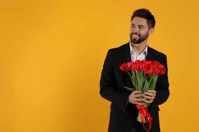 Photo of Happy man with red tulip bouquet on yellow background, space for text. 8th of March celebration