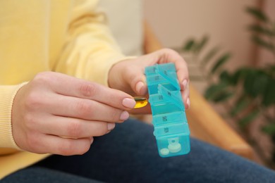 Photo of Woman taking pill from plastic box indoors, closeup
