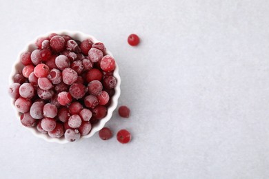 Frozen red cranberries in bowl on light table, top view. Space for text