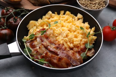 Delicious scrambled eggs with bacon in frying pan on grey table