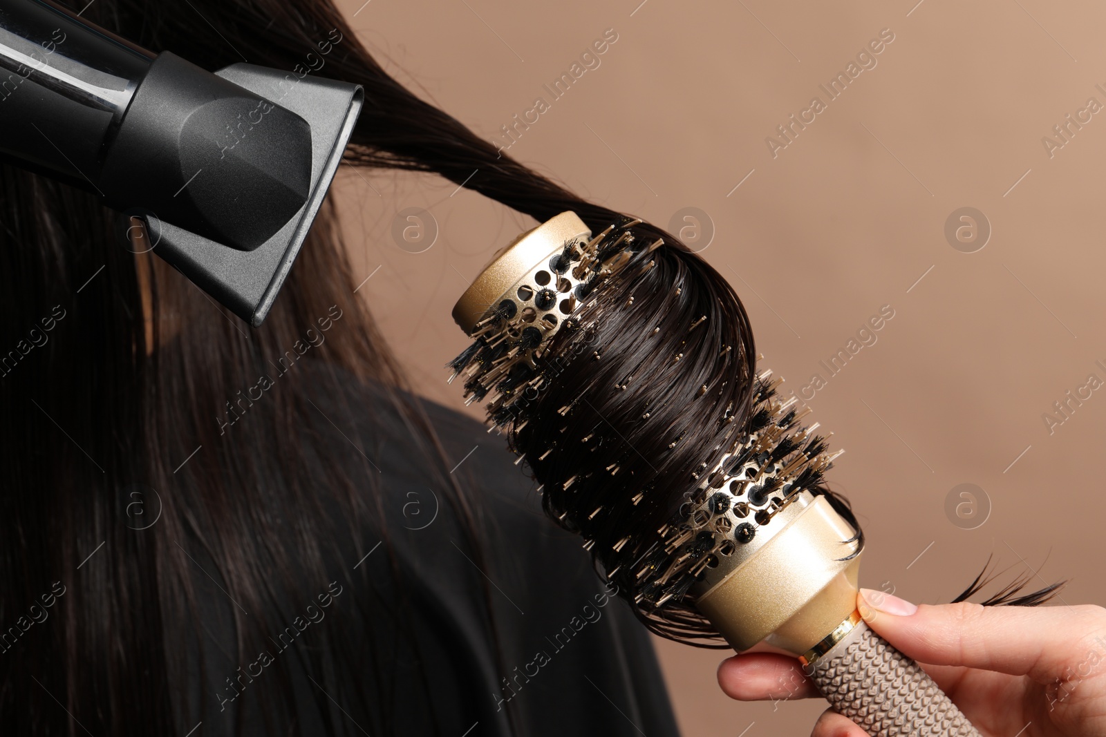 Photo of Hairdresser blow drying client's hair on light brown background, closeup