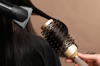Hairdresser blow drying client's hair on light brown background, closeup