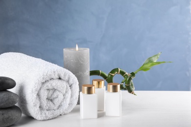 Spa stones, towel and bottles with cosmetic products on white wooden table