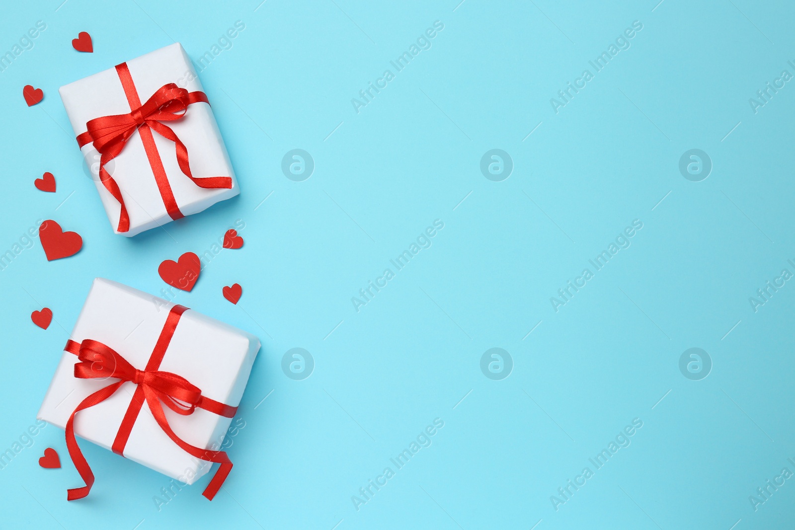 Photo of Beautiful gift boxes and red decorative hearts on light blue background, flat lay. Space for text