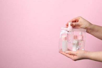 Cosmetic travel kit. Woman putting small bottle with personal care product into plastic bag against pink background, closeup. Space for text