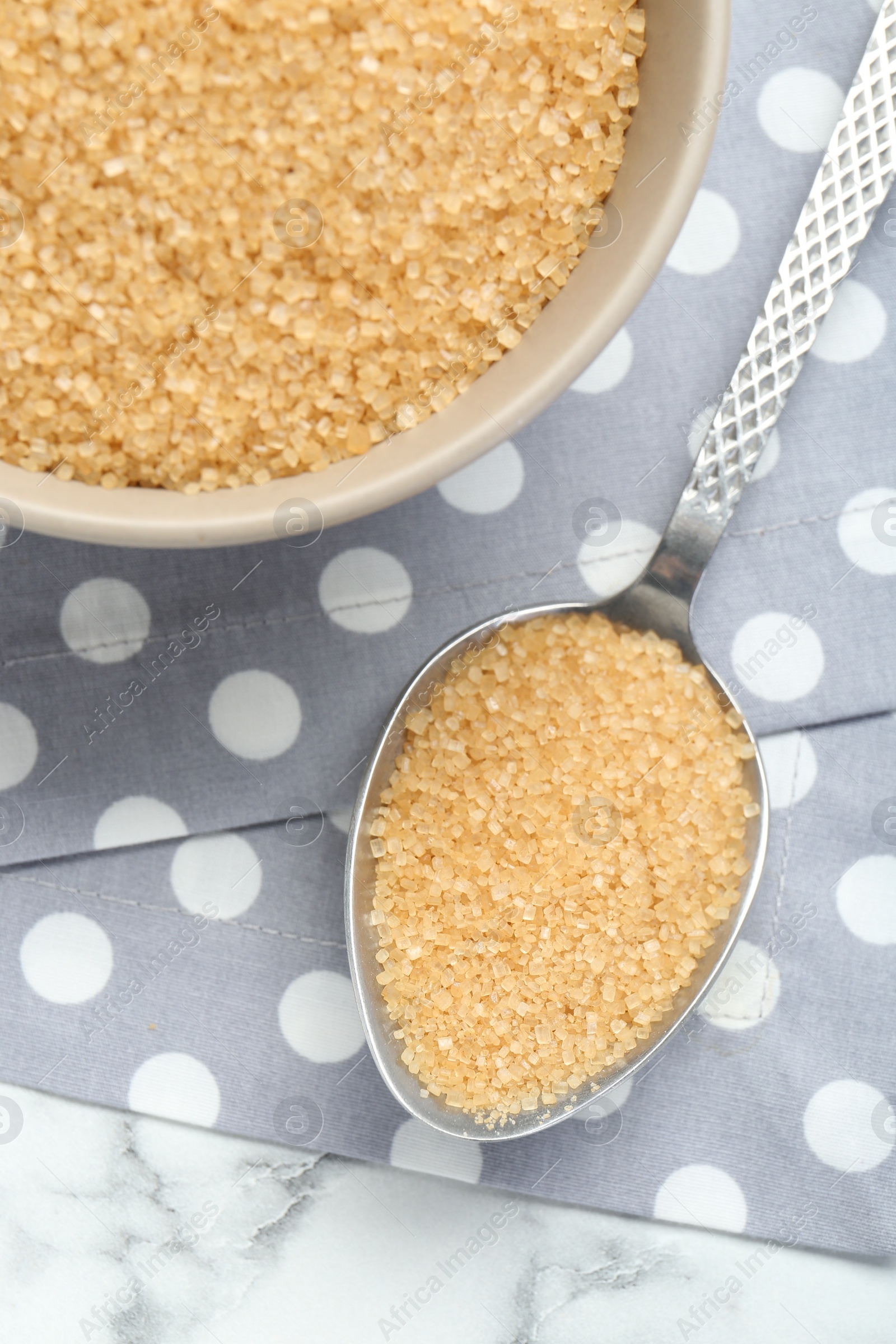 Photo of Brown sugar in bowl and spoon on white marble table, top view