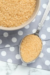 Brown sugar in bowl and spoon on white marble table, top view