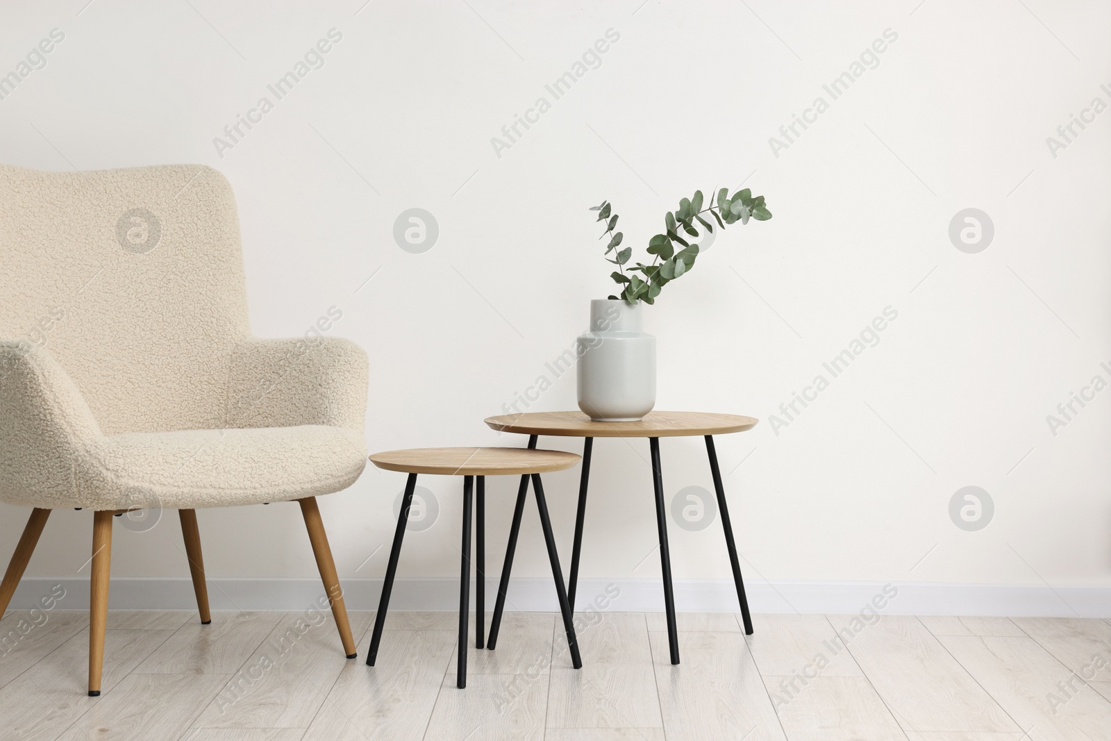 Photo of Comfortable armchair, nesting tables and eucalyptus indoors, space for text