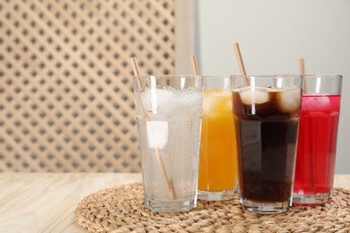 Glasses of different refreshing soda water with ice cubes and straws on wooden table, space for text