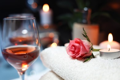 Photo of Rose and burning candle on towel near glasses of wine, closeup. Romantic bath