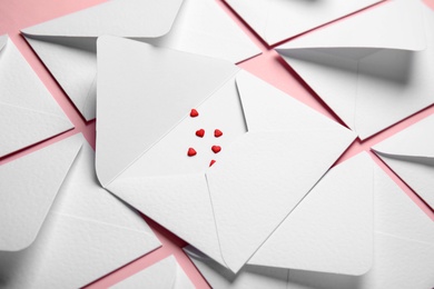 Envelopes and heart shaped sprinkles on pink background, closeup. Love letters